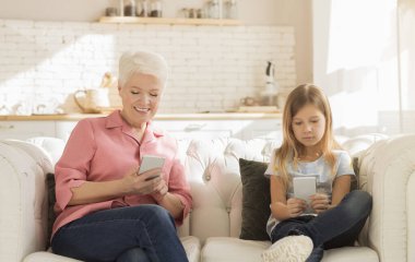 Gadget bağımlılığı. Olgun kadın ve torunu evde akıllı telefon kullanıyor.