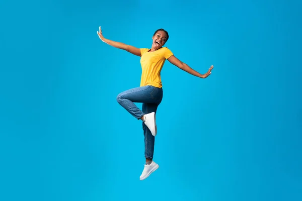 Позитивная афроамериканская девушка прыгает через синий фон — стоковое фото