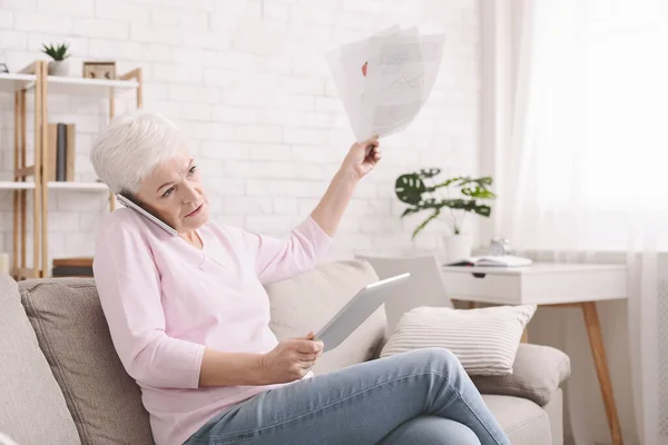 Décevante dame âgée lisant le document et parlant par téléphone — Photo