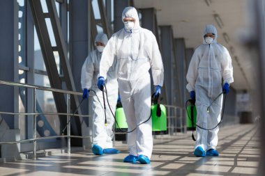 People in virus protective suits and mask disinfecting buildings clipart