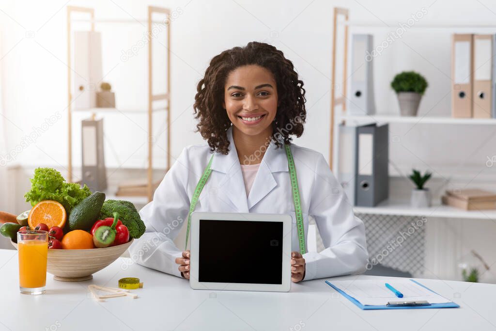 Smiling black nutritionist demonstrating digital tablet with empty screen