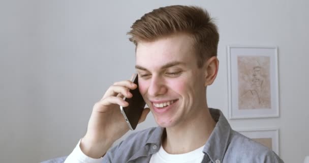 Молодой парень разговаривает дома на мобильном телефоне — стоковое видео