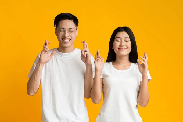 Jeune couple asiatique fermant les yeux et croisant les doigts avec espoir — Photo