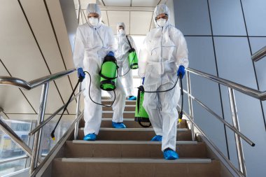 People wearing protective suits disinfecting stairs with spray clipart
