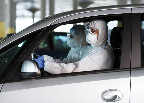 Pessoas em trajes de proteção coronavírus dirigindo um carro — Fotografia de Stock