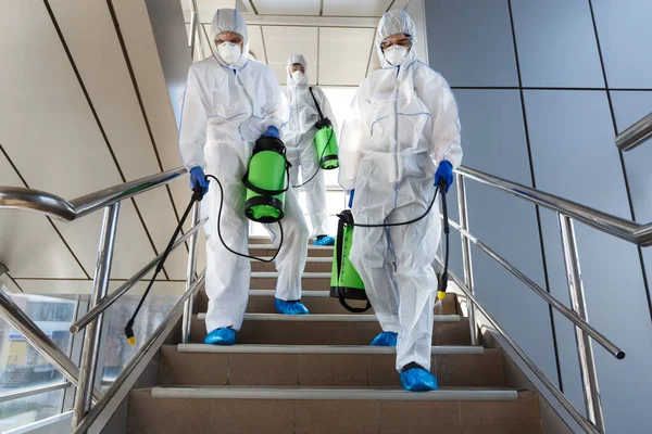 Mensen in beschermende pakken desinfecteren trappen met spray — Stockfoto