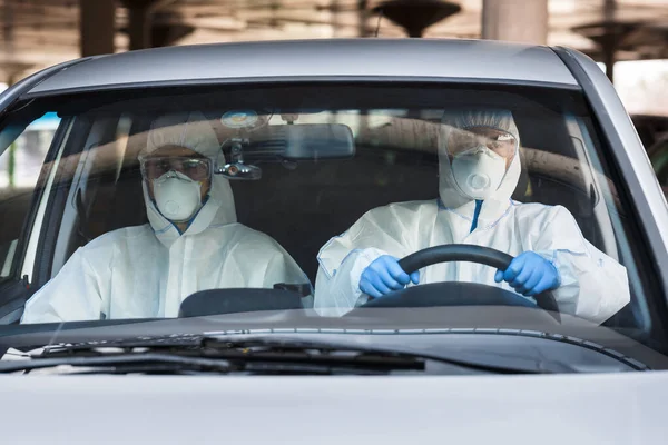 Two men in a car, both wearing virus protective suits — Stock Photo, Image
