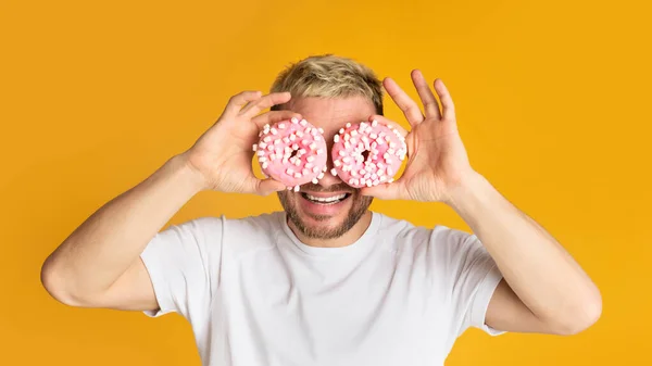 Homem segura donuts perto de seus olhos como óculos — Fotografia de Stock