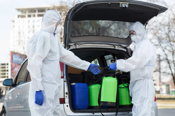 Pessoas em trajes protetores planejando fazer desinfecção com produtos químicos — Fotografia de Stock