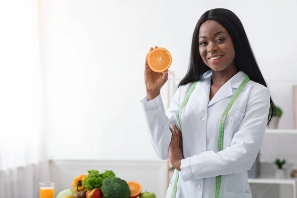 Femme noire nutritionniste positive tenant moitié orange — Photo