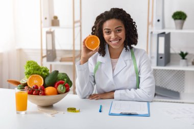Modern dietologist african woman recommending fresh oranges clipart