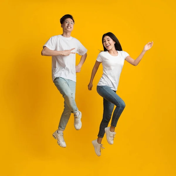 Zabawna azjatycka para szczęśliwie skacze po żółtym tle — Zdjęcie stockowe
