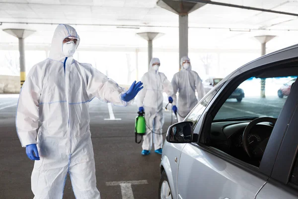 Hombres con trajes de materiales peligrosos deteniendo y desinfectando coches — Foto de Stock