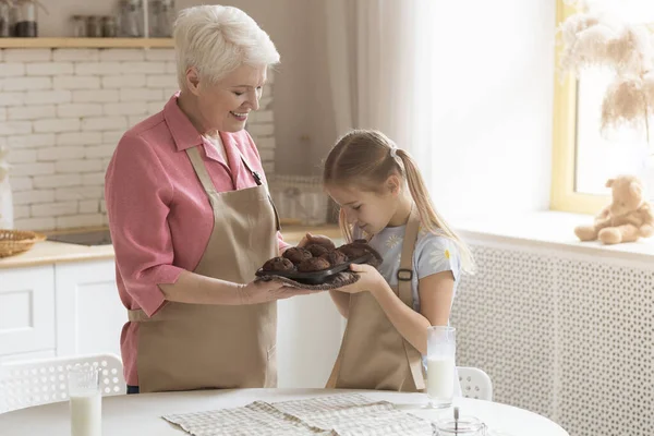 Ragazzina godendo aroma di muffin al cioccolato fresco con nonna in cucina, spazio vuoto — Foto Stock