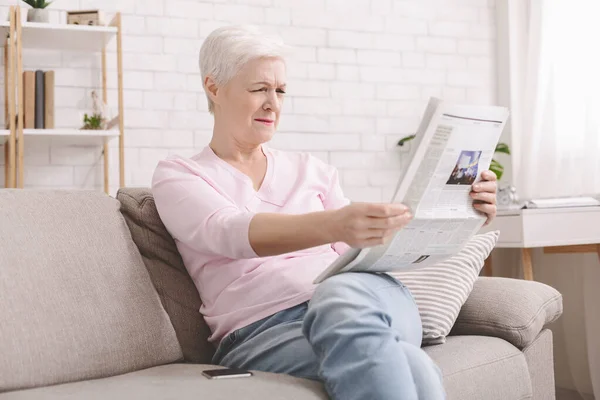 Idősebb hölgy hunyorog és tartja újság távol a szemét — Stock Fotó