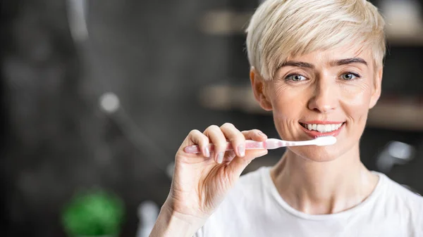 Утром веселая леди чистит зубы зубной щеткой в ванной комнате — стоковое фото