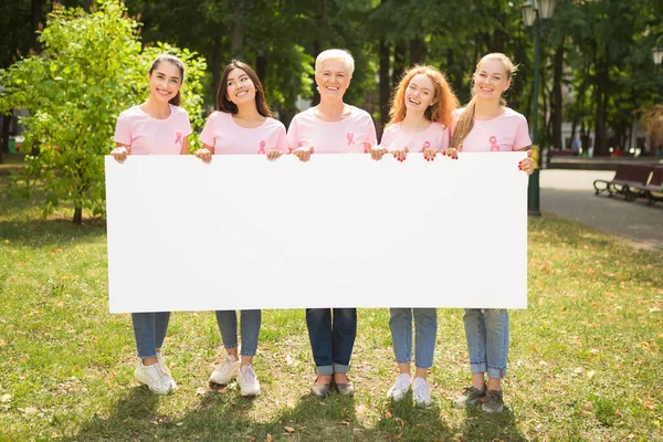 Mujeres con cintas de cáncer sosteniendo cartel posando en el parque, burla —  Fotos de Stock