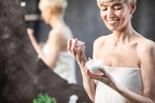 Усміхнена жінка відкриває крем для обличчя стоячи у ванній вдома — стокове фото