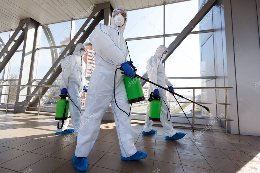Men in respirators and protective suits cleaning public places with chemicals
