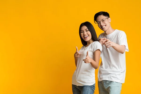Przyjazna azjatycka para wskazująca przed kamerą na żółtym tle — Zdjęcie stockowe