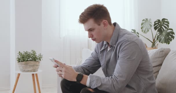 Раздражённый молодой человек, работающий по мобильному телефону дома — стоковое видео
