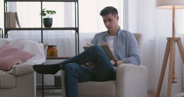 Jovem lendo livro em casa, virando próxima página — Vídeo de Stock