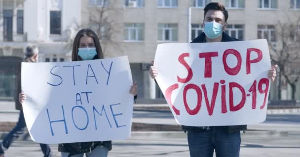 Giovane uomo e donna in piedi con cartelli SOGGIORNO A casa e fermare COVID-19 — Video Stock