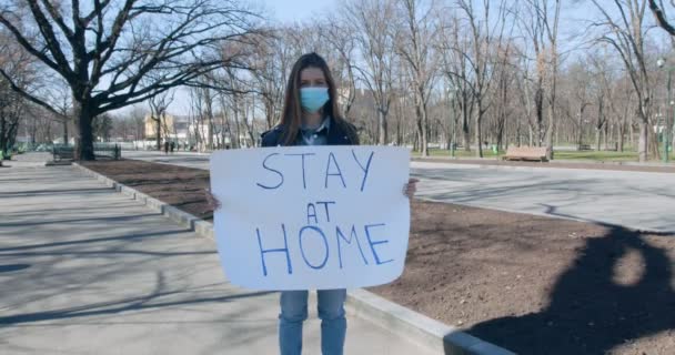 Девушка в защитной маске держит плакат дома — стоковое видео