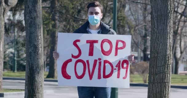 Młody mężczyzna w masce ochronnej z plakatem Stop COVID-19 — Wideo stockowe