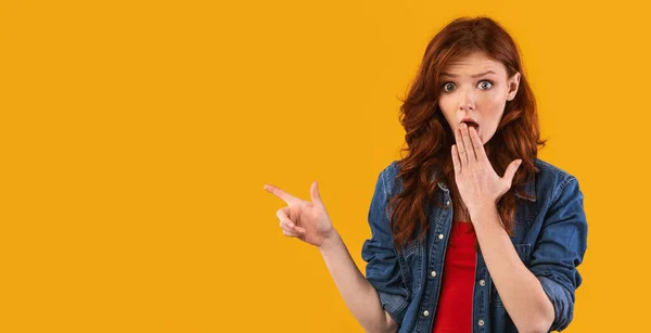 Shocked chica señalando los dedos a un lado cubriendo la boca en el fondo amarillo —  Fotos de Stock