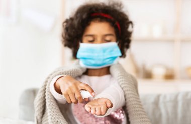 Coronavirus önleme. Küçük Afrikalı Amerikalı kız evdeki ellerine dezenfektan sürüyor.
