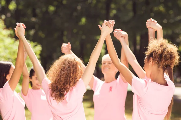 Vrouwelijke vrijwilligers ondersteunen oncologie bewustmakingscampagne die handen in de buitenlucht houdt — Stockfoto