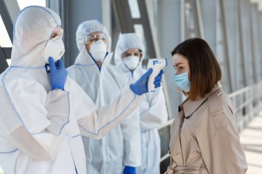 Medical workers in protective suits measuring temperature clipart