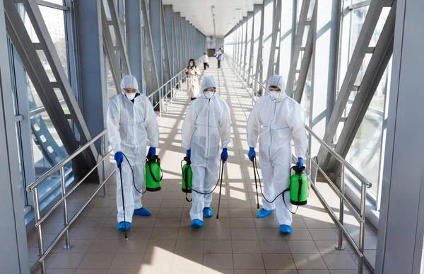 Especialistas en trajes de materiales peligrosos haciendo desinfección de lugares públicos —  Fotos de Stock