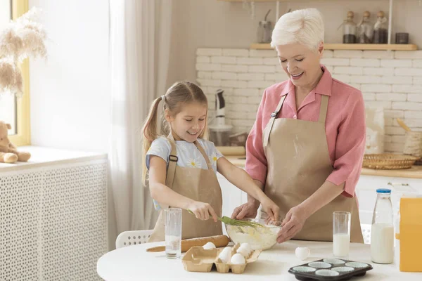Cuisiner avec mamie est amusant. Femme plus âgée et petite-fille mélangeant la pâte pour la pâtisserie ensemble dans la cuisine, espace de copie — Photo
