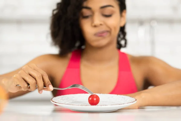 Афро-женщина смотрит на крошечный помидор на тарелке — стоковое фото