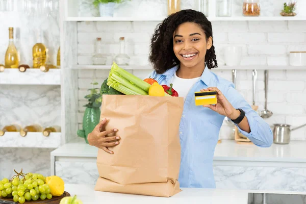 Черная девушка показывает кредитку и бумажный пакет с едой — стоковое фото