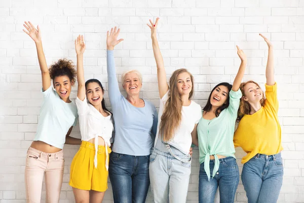 Señoras multiétnicas agitando las manos posando contra el fondo de la pared de ladrillo blanco — Foto de Stock