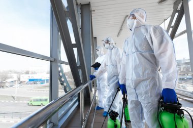 Tehlikeli madde giysileri içinde sağlık görevlileri halka açık yerlere sprey sıkarak dezenfekte ediyorlar.