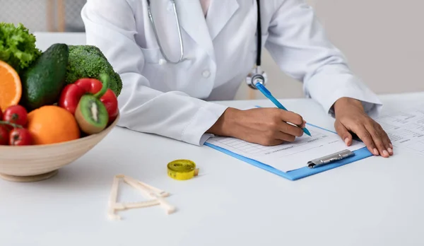 Cropped of dietologist workplace, african woman doctor making prescription — Stock Photo, Image