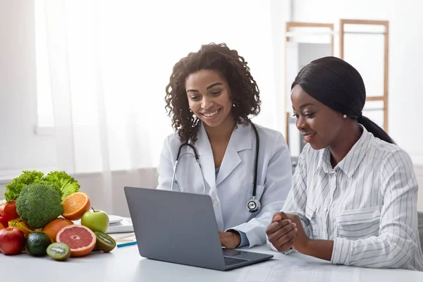 Nutrizionista sorridente che mostra informazioni sui pazienti sul computer portatile — Foto Stock