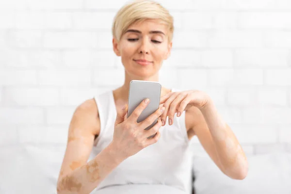 Cheerful middle aged lady texting on modern cellphone