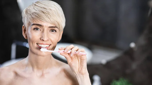 Уборка зубов леди улыбается на камеру в ванной комнате, Панорама — стоковое фото