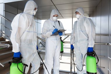 Virüs korumalı giysiler giyen adamlar ev içi konaklamayı dezenfekte ediyorlar
