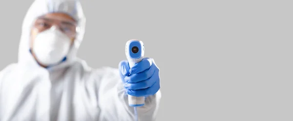 Азиатский человек в защитном костюме, медицинской маске и очках измеряет температуру — стоковое фото
