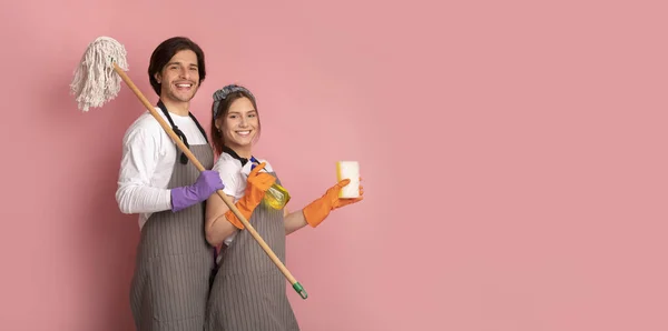 Felice Janitors coppia in grembiuli con forniture per la pulizia su sfondo rosa — Foto Stock