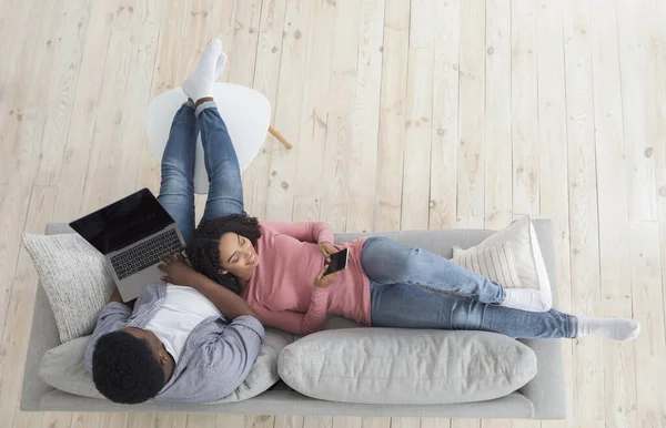 Feliz casal preto passar tempo em casa com laptop e smartphone — Fotografia de Stock