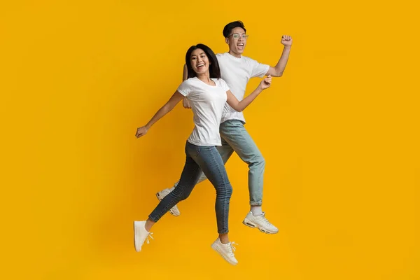 Sarı arka planda hızla koşan mutlu Asyalı çift — Stok fotoğraf