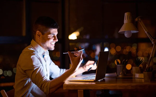 Uomo d'affari sorridente che utilizza assistente vocale nell'ufficio moderno di notte — Foto Stock