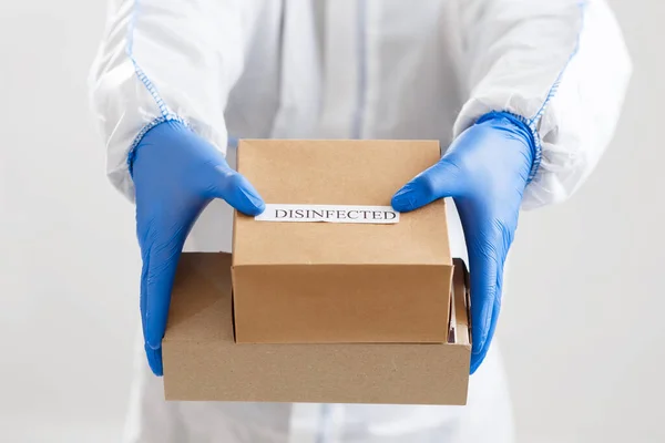 Egy férfi védőruhában és kesztyűben fertőtlenített dobozokat ad. — Stock Fotó